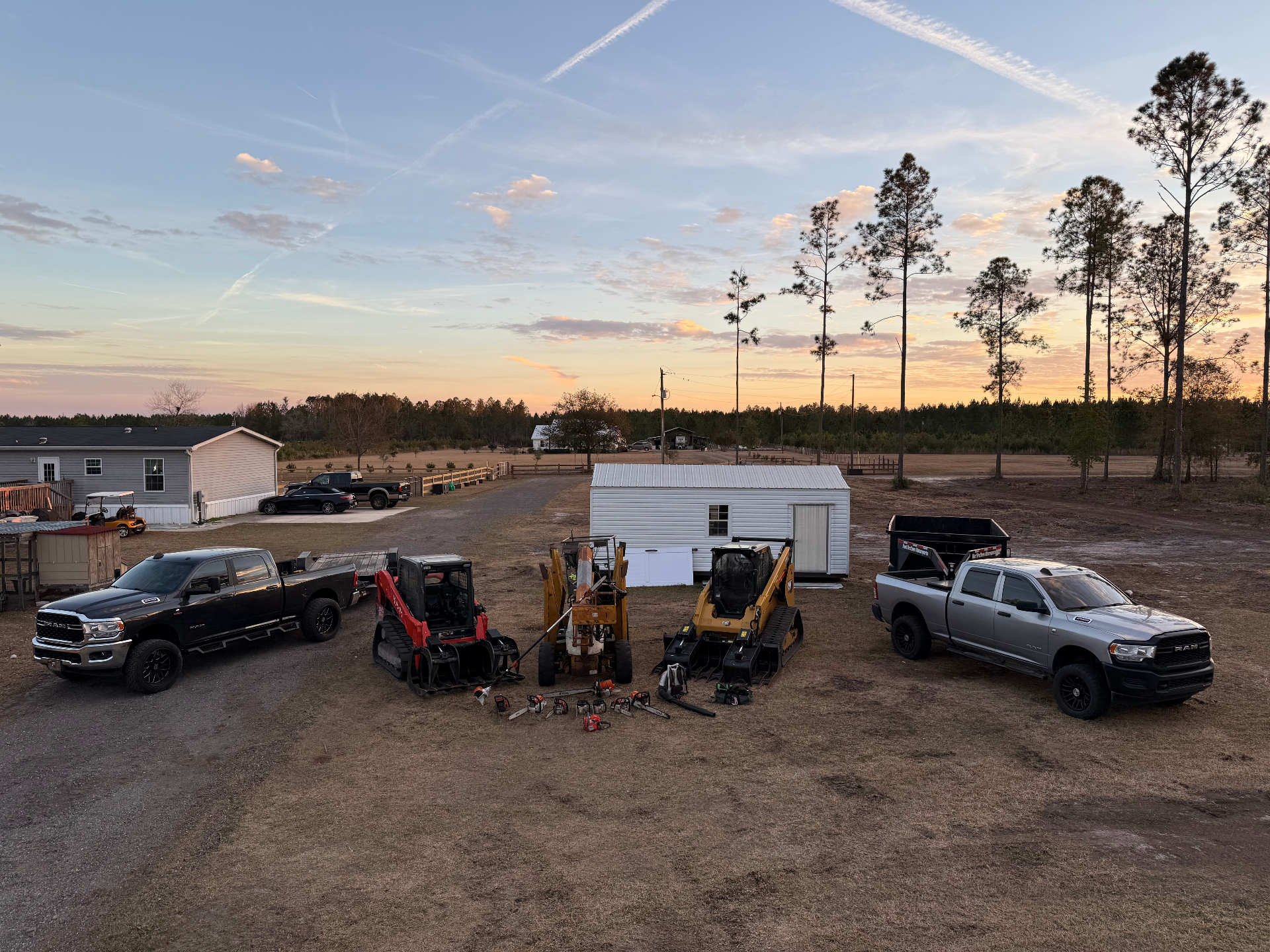 AGES Tree Service full fleet and equipment lineup at sunset including trucks skid steers and chainsaws