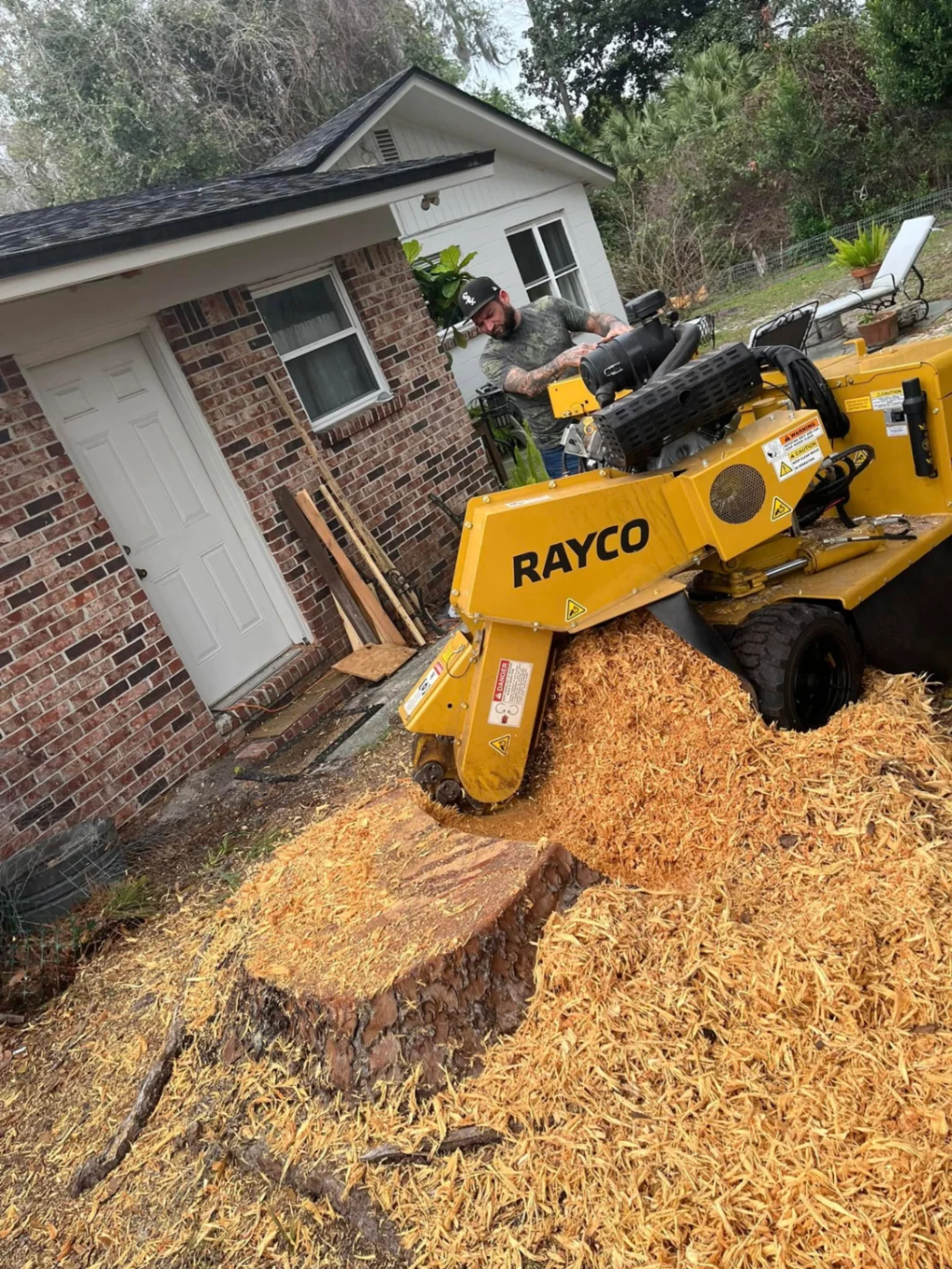 AGES Tree Service operator grinding large stump with Rayco machine near residential home in Orange Park FL
